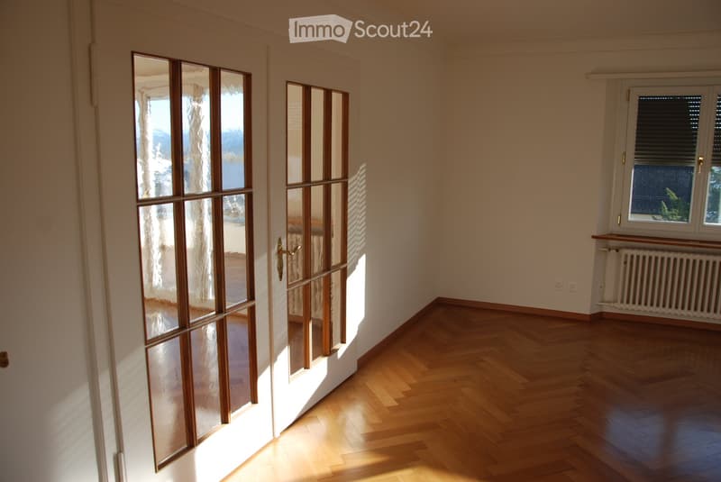 Empty room with wooden flooring, large glass doors leading outside, and a window with blinds.