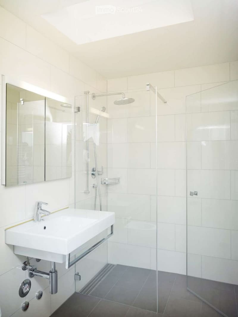 Modern bathroom with white tiles, a white sink, a large mirror, and a glass-enclosed shower with a modern showerhead.
