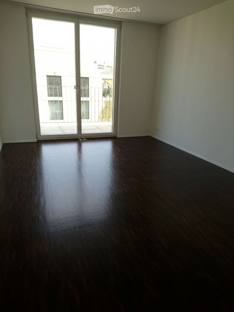 Empty room with dark wooden flooring and large sliding glass doors leading to a balcony.