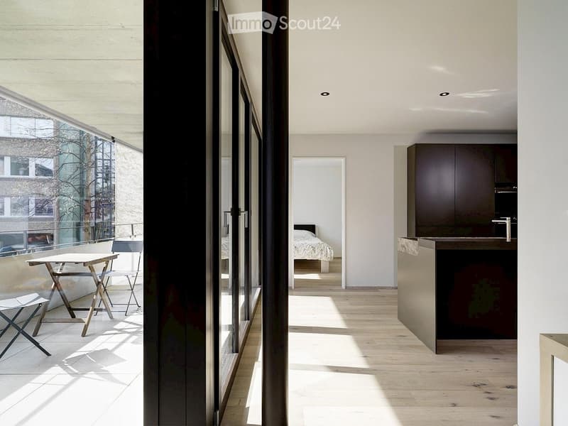 Modern, open-plan living space with a kitchen area, a bedroom visible through a doorway, and a small outdoor seating area with a table and chairs.