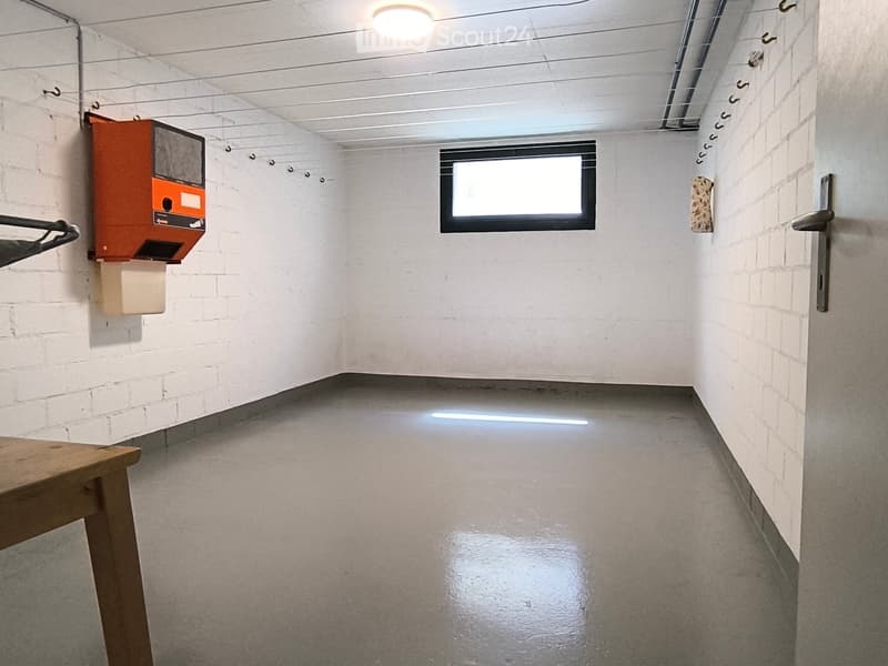 Empty room with white brick walls, concrete floor, single window, and a small wooden bench near the door.