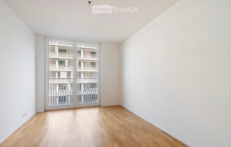 Empty room with light wooden flooring and white walls, featuring a large sliding glass door leading to a balcony.