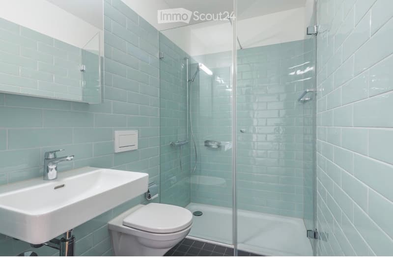 Modern bathroom with light blue tiles, a white sink with a chrome faucet, a toilet, and a glass-enclosed shower with a modern showerhead.