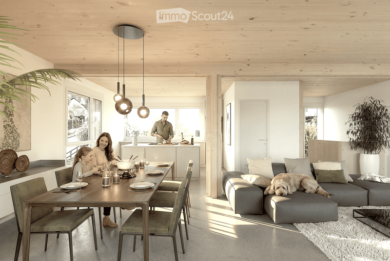 Open-plan living and dining area with a grey sectional sofa, wooden dining table with chairs, pendant lights, and a kitchen island in the background.
