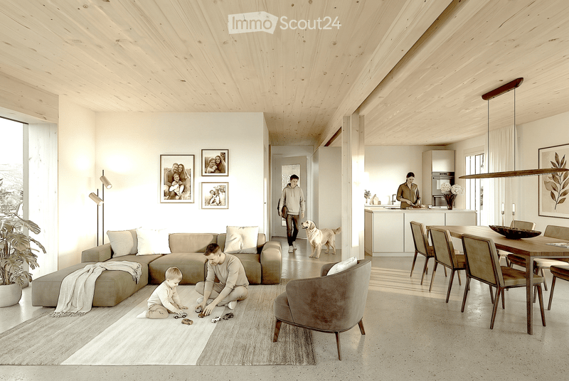 Open-plan living and dining area with light wood ceilings, white walls, and large windows. Features a sectional sofa, armchair, dining table with chairs, kitchen counter, and decorative elements like framed photos and a potted plant.
