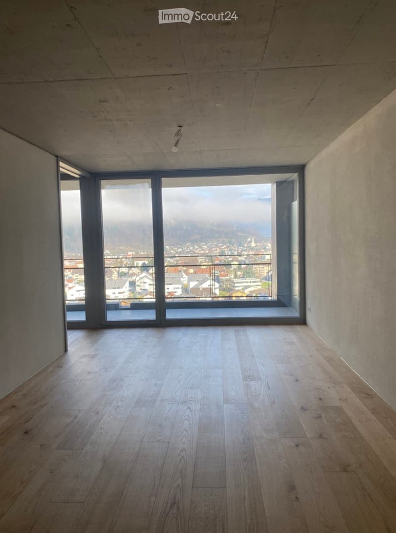 Empty room with wooden flooring, large windows offering a scenic view, and a modern, minimalist design.