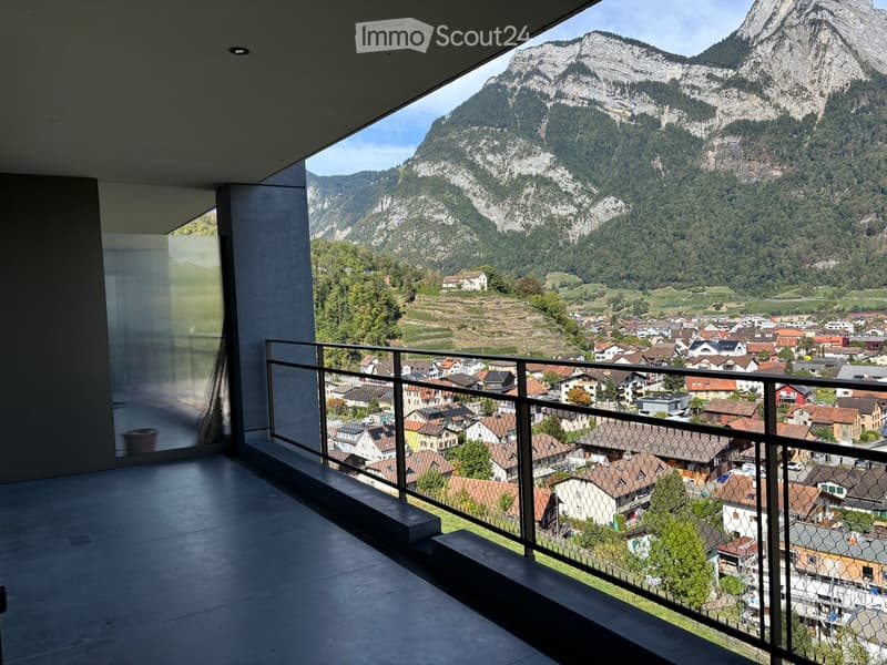 Modern balcony with a metal railing, overlooking a town and mountain landscape.