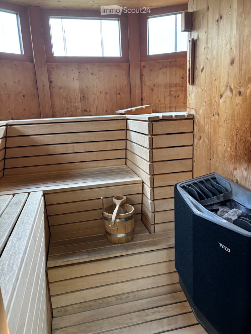 Wooden sauna with benches, a wooden bucket, and a wooden paddle, natural light from small windows.