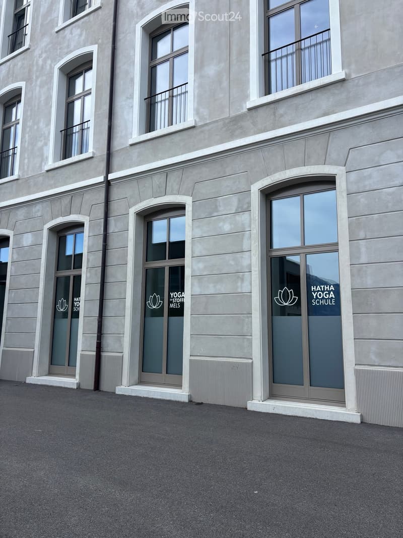 Modern building facade with large windows and arched doorways, featuring yoga school signage.