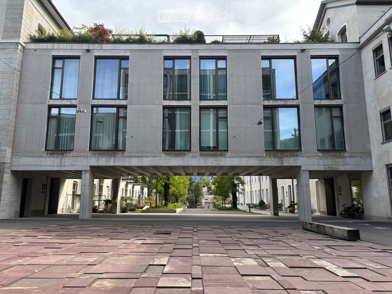 Modern two-story building with large windows, raised ground floor, and a rooftop garden area.