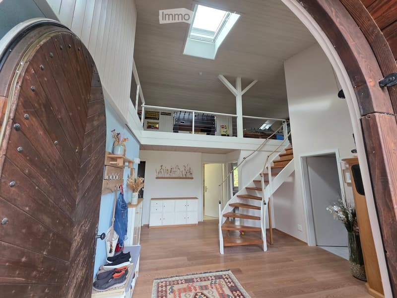 Spacious hallway with wooden flooring, white walls, and a staircase leading to an upper level. Features include a coat rack, small shelves, and a decorative rug on the floor.