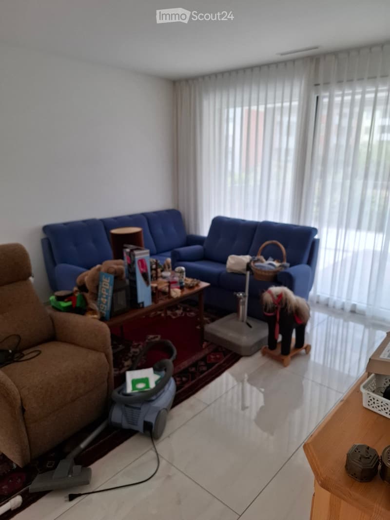 A cozy living room with a blue sofa, a wooden coffee table, a brown armchair, a toy horse, and a vacuum cleaner on the floor.