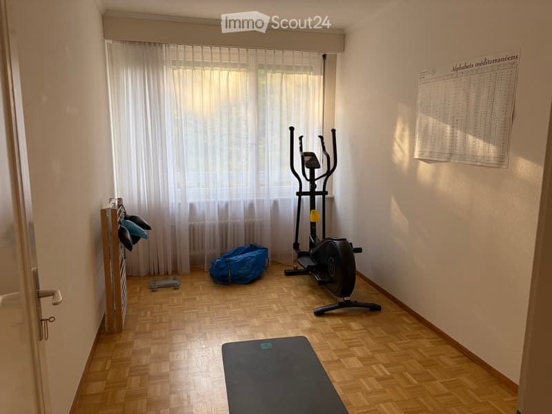 Exercise room with wooden flooring, exercise bike, yoga mat, scale, coat rack, and a blue bag.