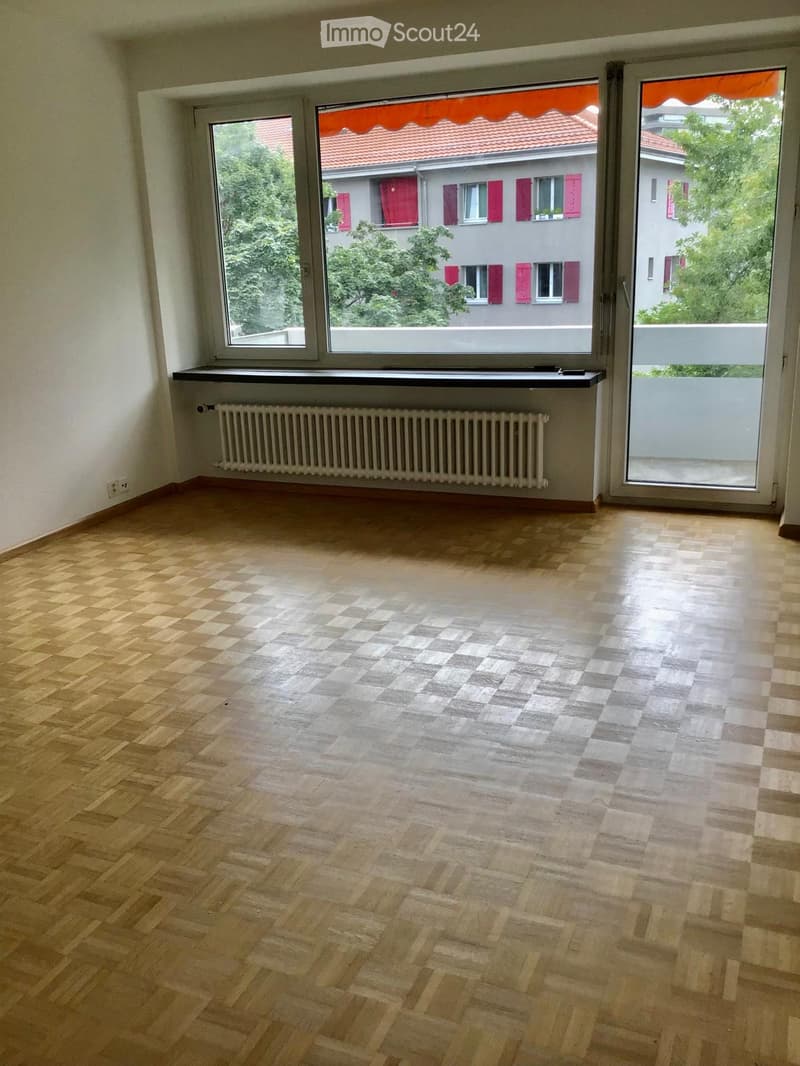 Empty room with wooden flooring, large windows, radiator, and sliding glass door leading to a balcony.