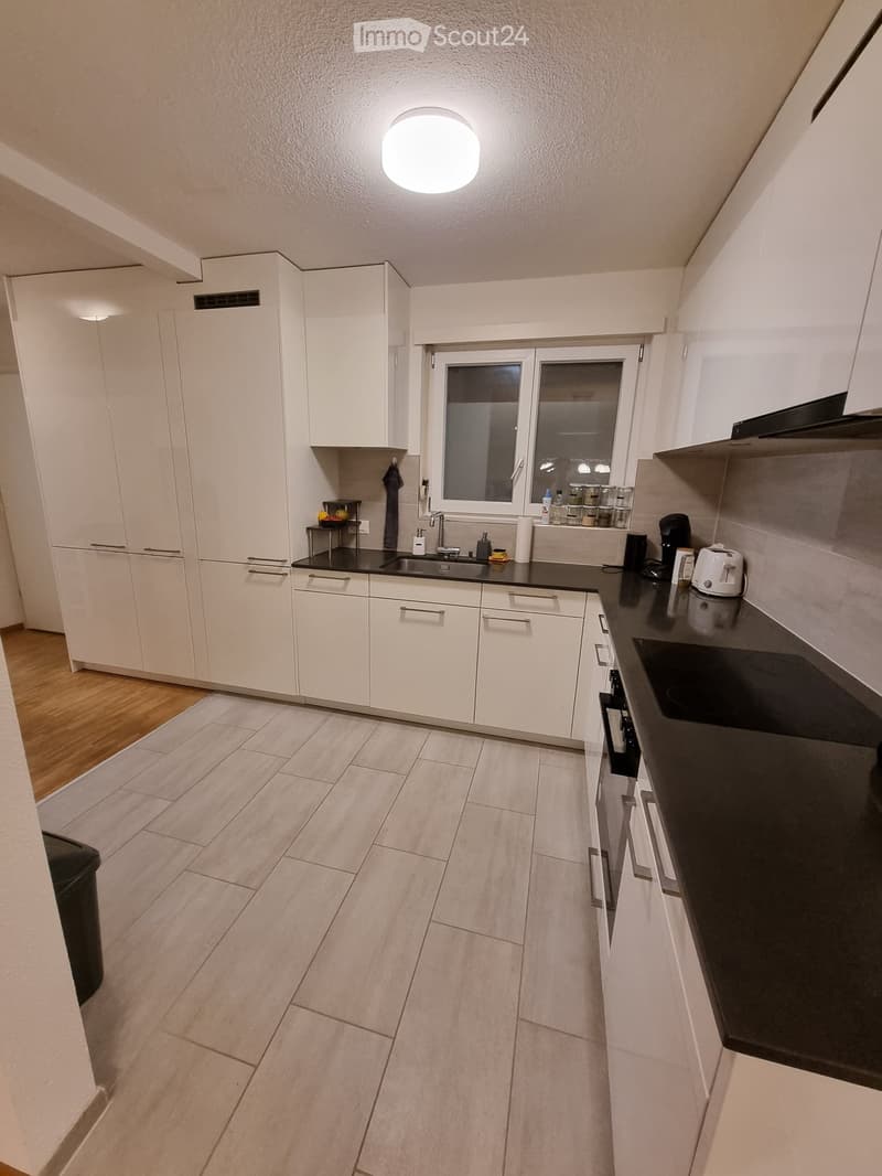 Modern kitchen with white cabinets, black countertops, and a window above the sink. Includes a sink, faucet, toaster, coffee maker, and various small appliances.