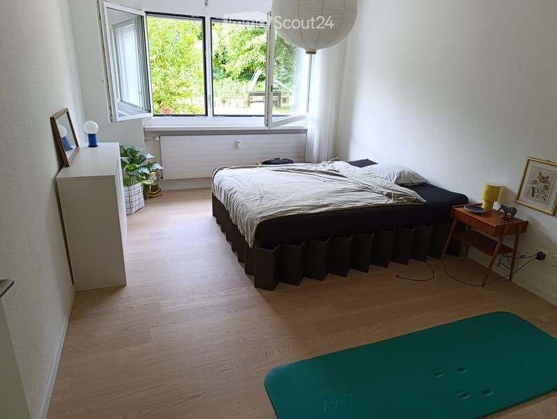 Modern bedroom with a large bed, nightstands, lamps, a potted plant, and a yoga mat on the floor.