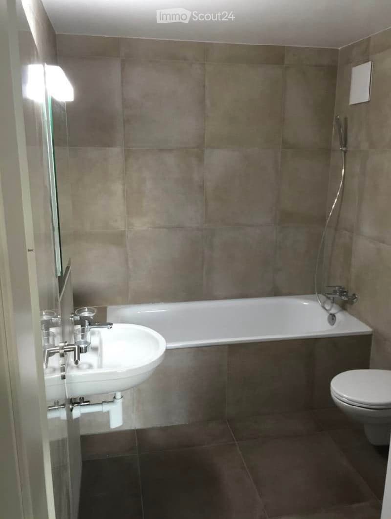 Modern bathroom with a white sink, bathtub, and toilet, featuring a glass shower enclosure and tiled walls.
