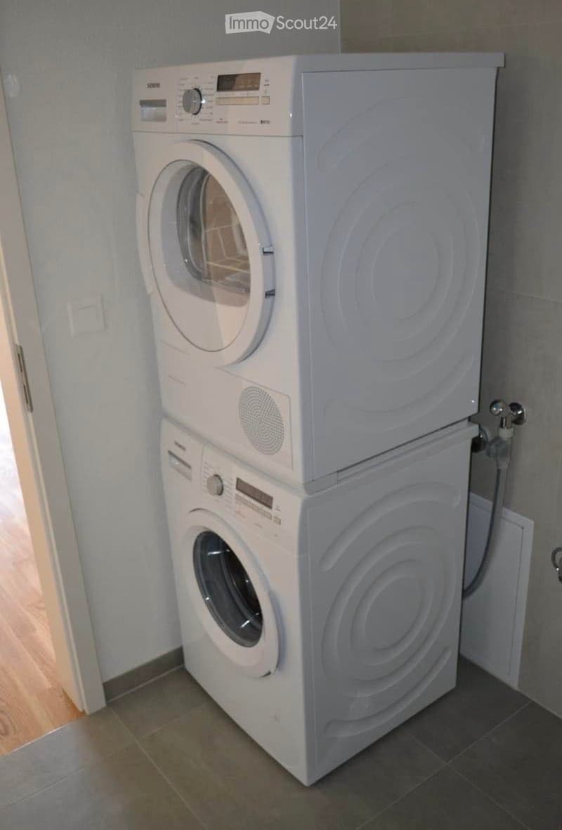 A compact bathroom with a stacked washing machine and dryer unit, featuring a tiled floor and light-colored walls.