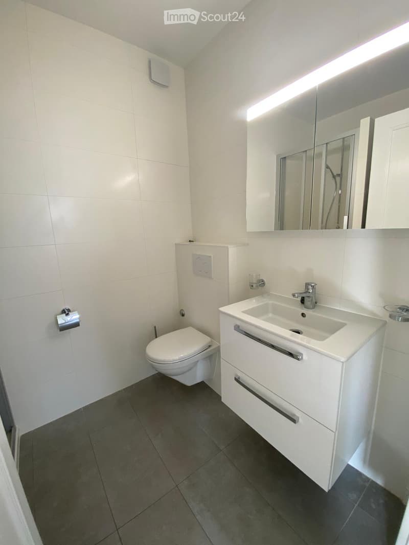 Modern bathroom with white tiles, a toilet, a sink with a mirror, and a cup on the sink counter.
