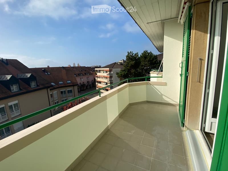 Balcony with tiled floor, green metal railing, and view of neighboring buildings and trees.