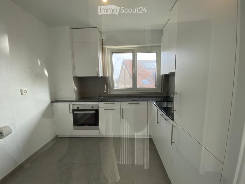 Modern kitchen with white cabinets, black countertop, and built-in oven. Features tiled flooring and large windows with a view of neighboring buildings.