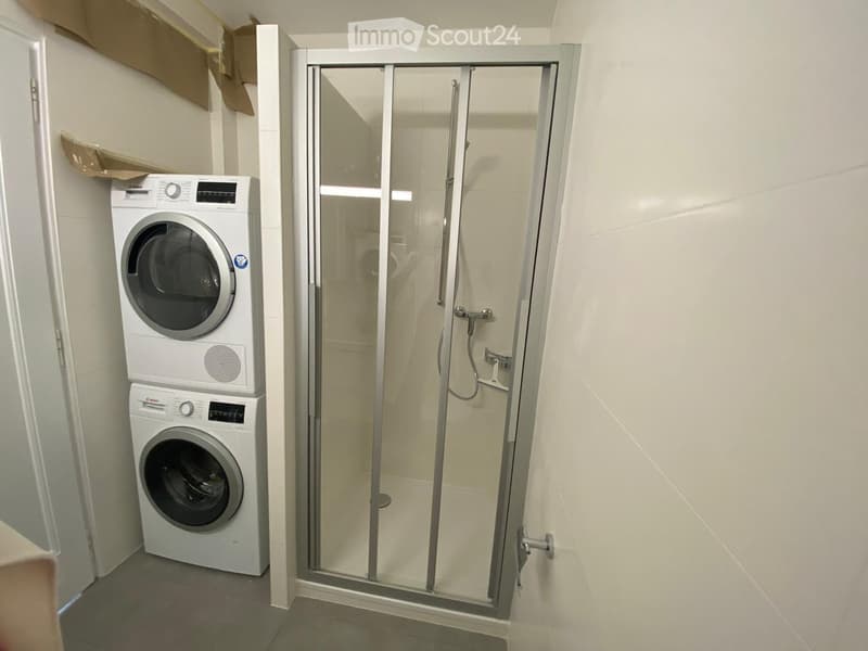Bathroom with a glass-enclosed shower and a stacked washing machine and dryer unit.
