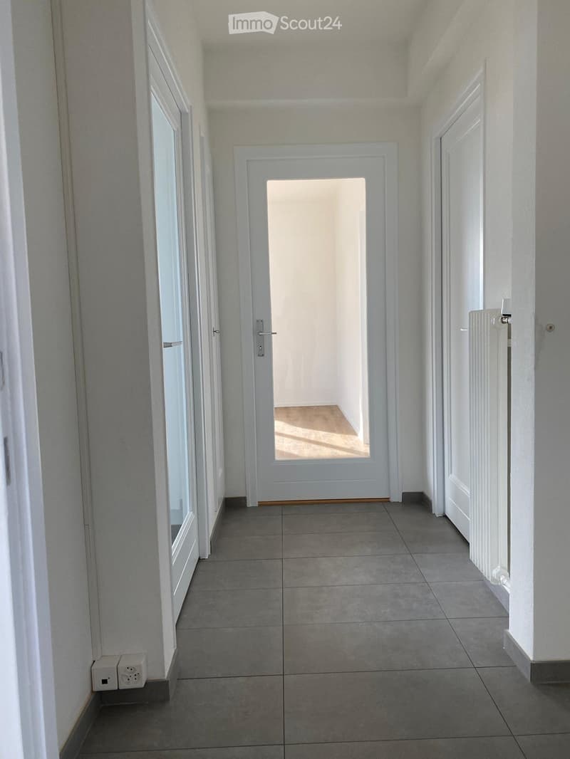 Empty hallway with tiled floor, white walls, and multiple doors including a glass-paned door at the end.