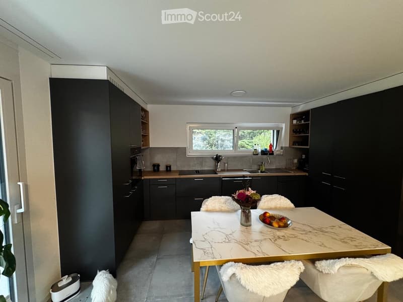 Modern kitchen with dark cabinets, a marble dining table, and four white chairs with fur cushions. The kitchen features a window, a sink, and a dishwasher.