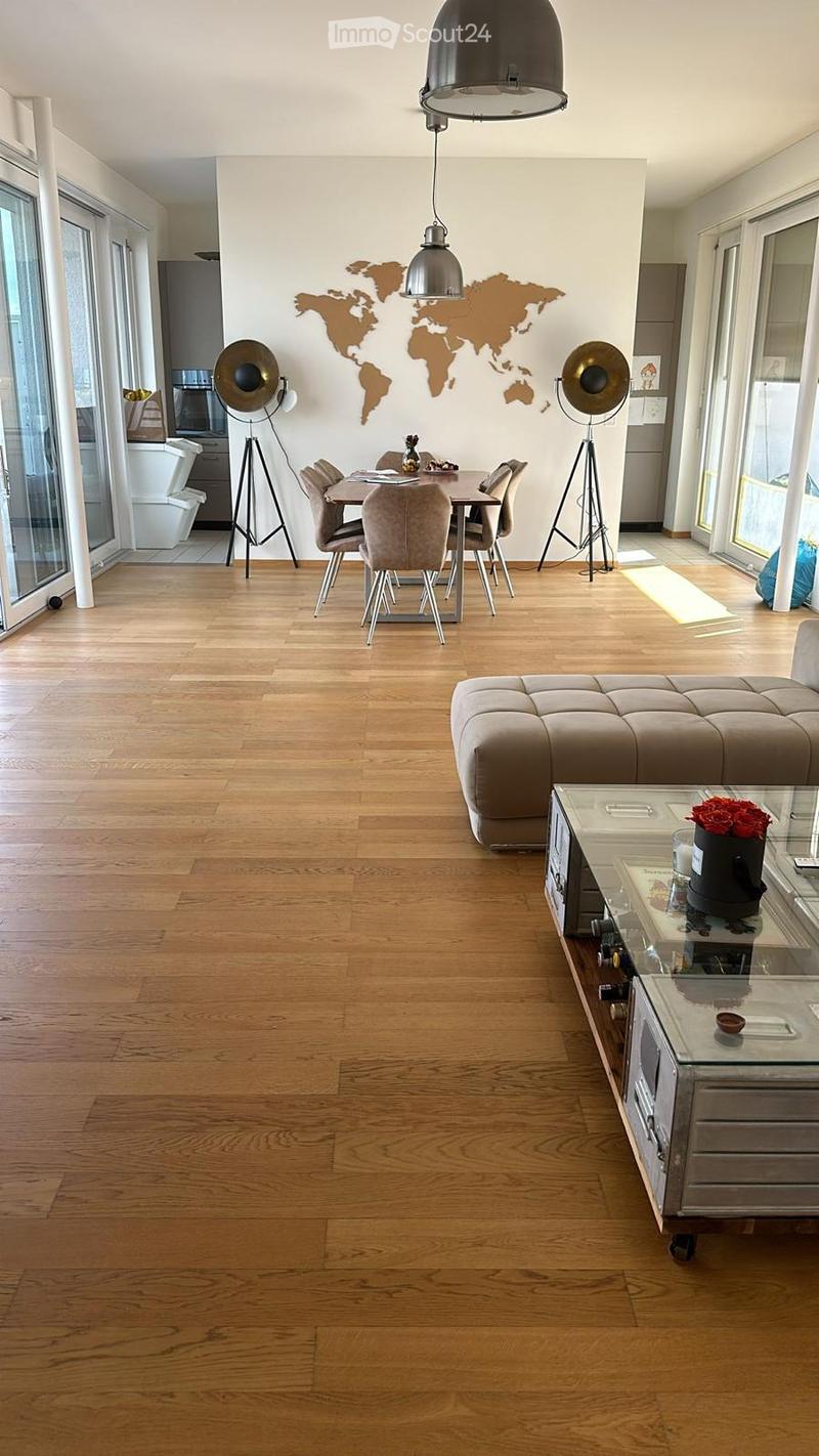 Open-plan living and dining area with wooden flooring, a large sofa, a coffee table, a dining table with chairs, pendant lights, and floor lamps.