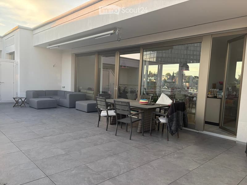 Balcony with tiled floor, grey sofa, ottoman, dining table, and chairs.