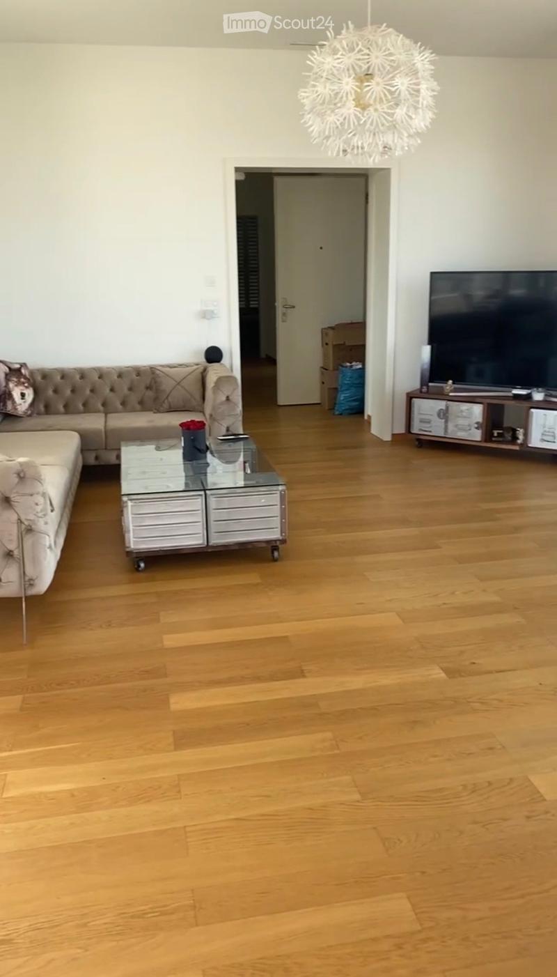 Modern living room with light wooden flooring, a beige tufted sofa, a glass coffee table, and a flat-screen TV on a wooden stand.