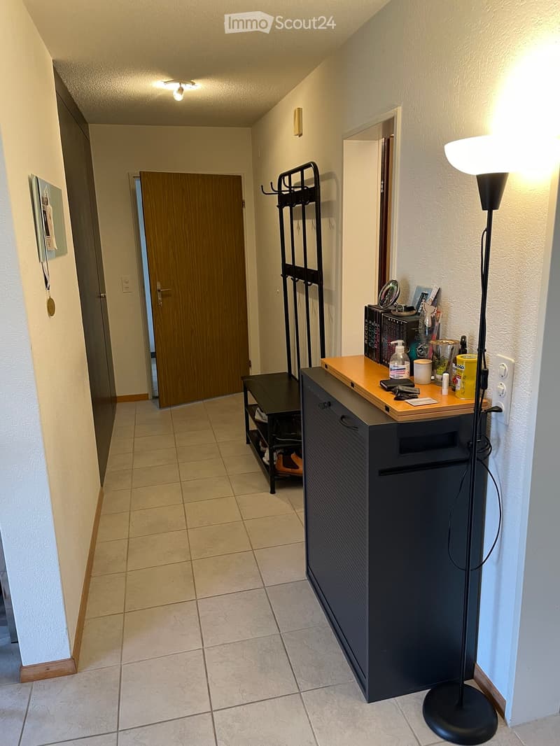 Hallway with tiled floor, wooden door, coat rack, small table with items, and floor lamp.