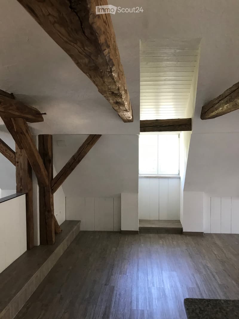 Staircase with wooden beams and steps, white walls, and a window at the top, leading to an open space with wooden flooring.