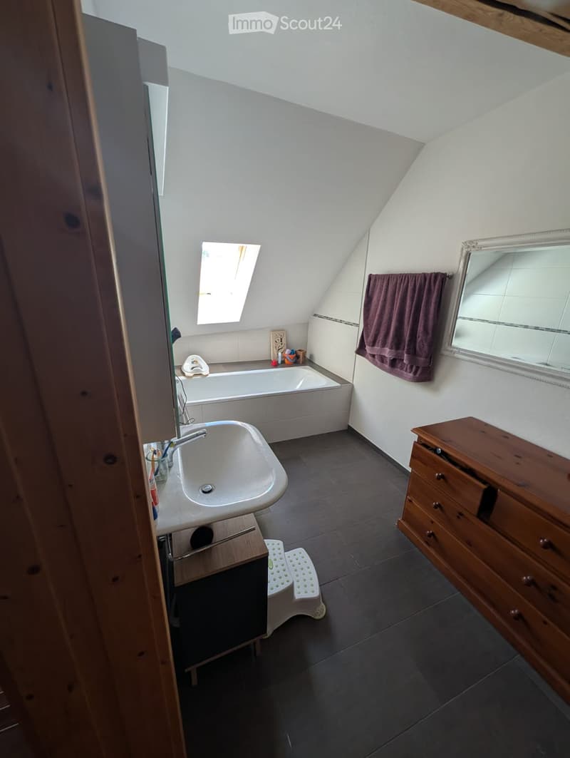 Bathroom with a bathtub, sink, mirror, and wooden cabinet. Features a skylight window and a towel hanging on the wall.
