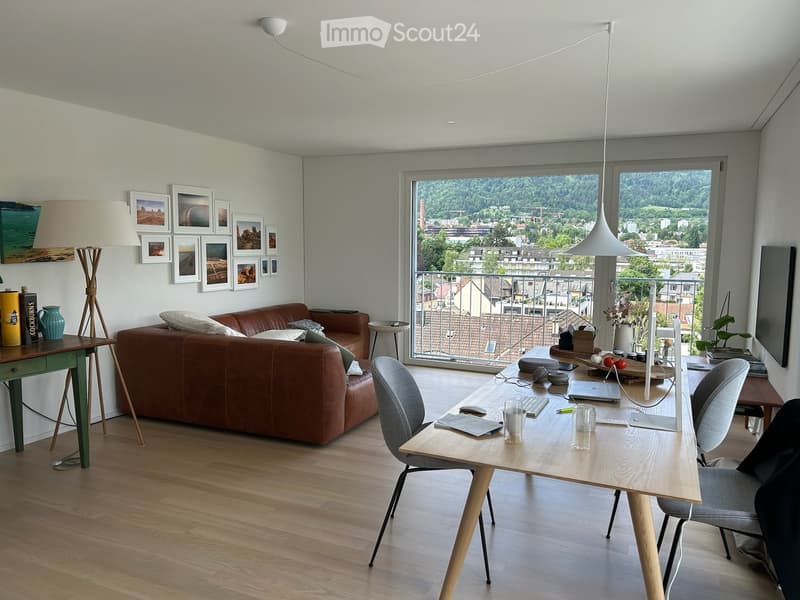 Modern living room with a brown leather sofa, wooden table, chairs, laptop, and a view of the city from large windows.