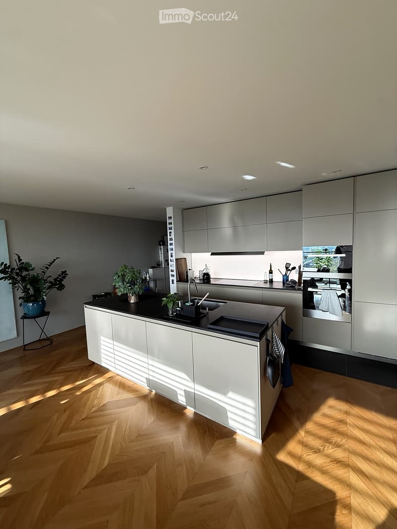 Modern kitchen with white cabinets, black countertop, wooden floor, and various appliances and utensils.
