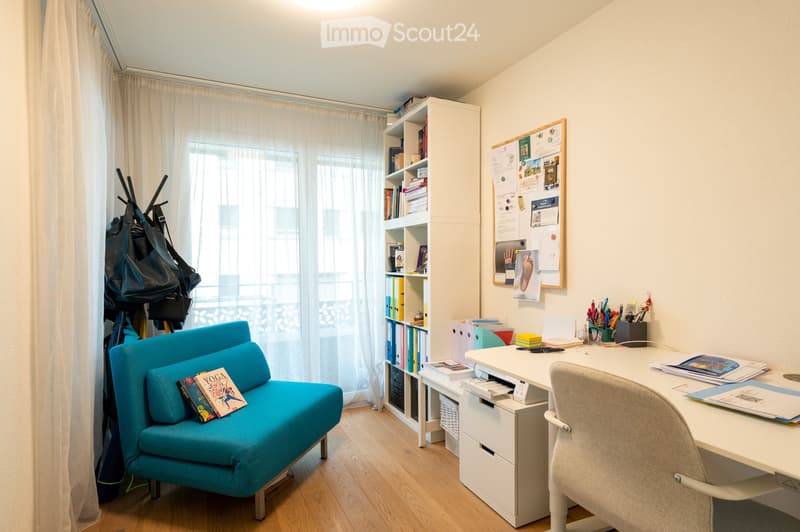 workspace with desk, bookshelf, small sofa, large window, storage bags, papers