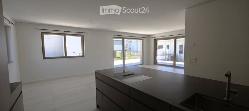 Modern kitchen with dark countertops, built-in sink, and large windows and sliding doors leading to a balcony.