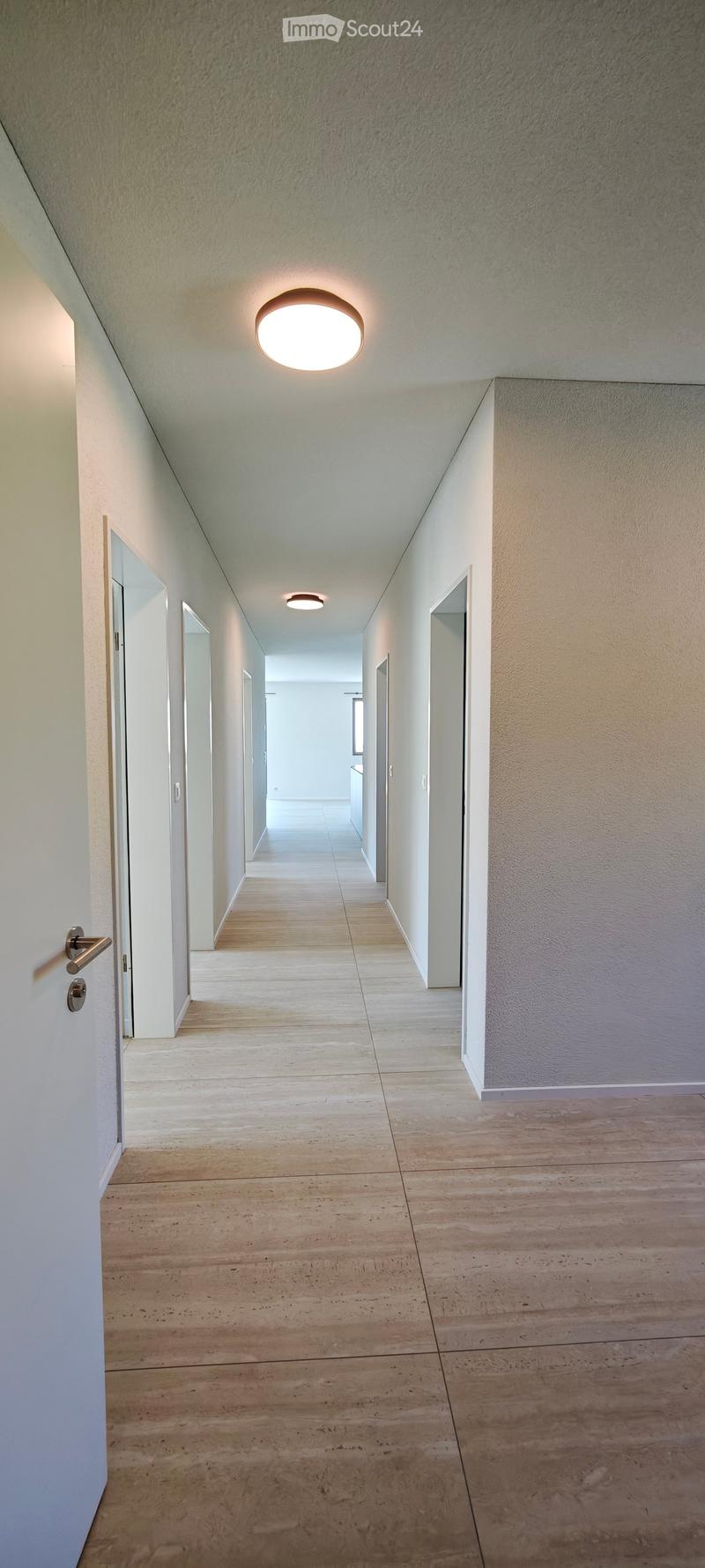 Clean, modern hallway with wooden flooring, white walls, and recessed lighting. Doors are visible on both sides, leading to other rooms.