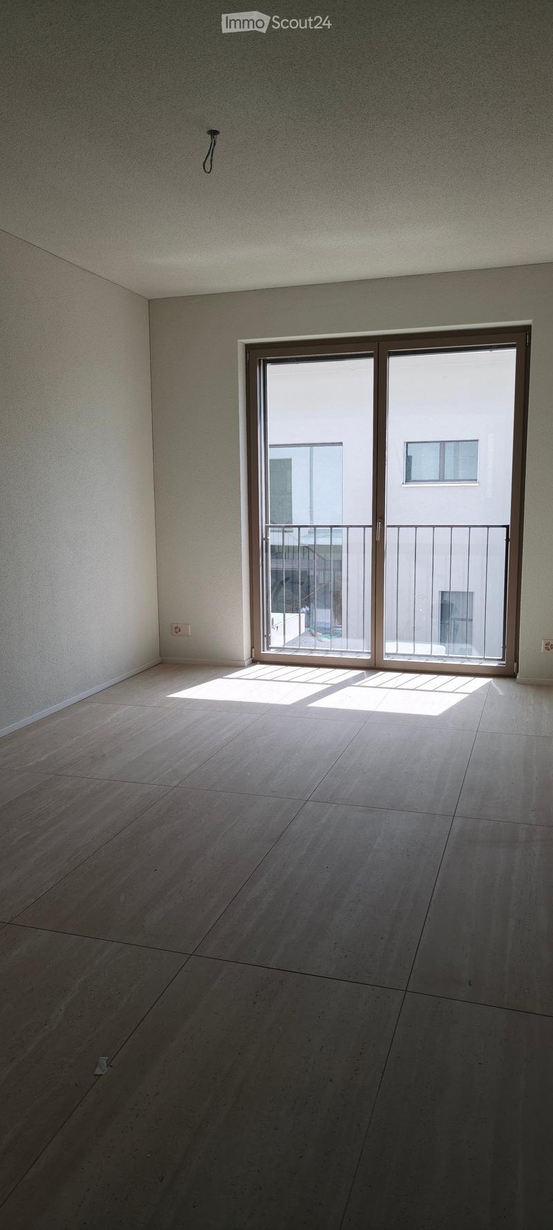 Empty room with light-colored tiled floor and white walls, featuring a large sliding glass door leading to a balcony.