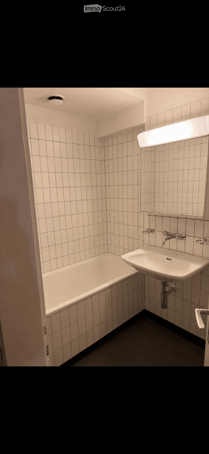 Modern bathroom with white tiled walls, a bathtub, a sink with a modern faucet, and a large mirror with built-in lighting.