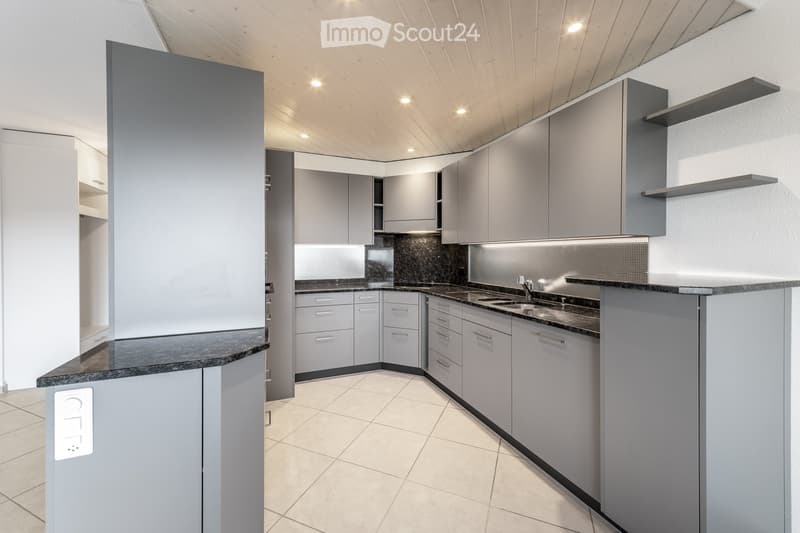 Modern kitchen with grey cabinets, dark countertops, and a sleek design. Features include a sink, faucet, and built-in storage with shelves.