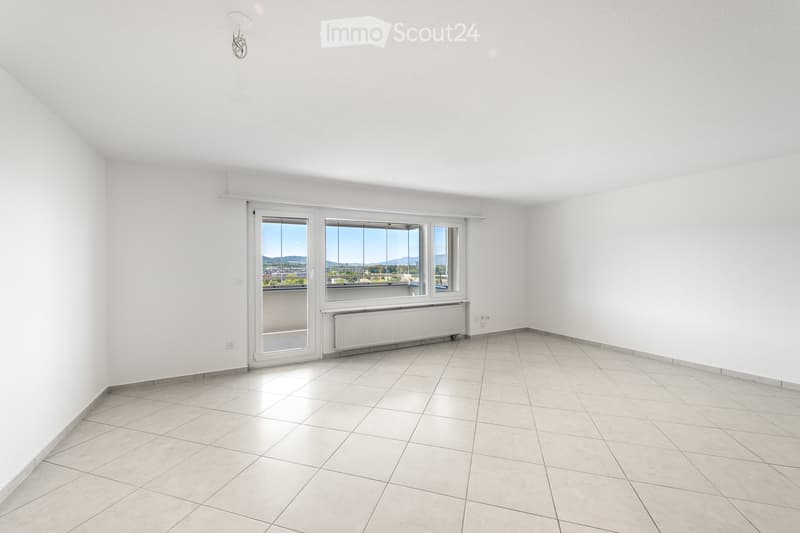 Empty room with white walls, tiled floor, large windows, and a radiator. No furniture or equipment present.