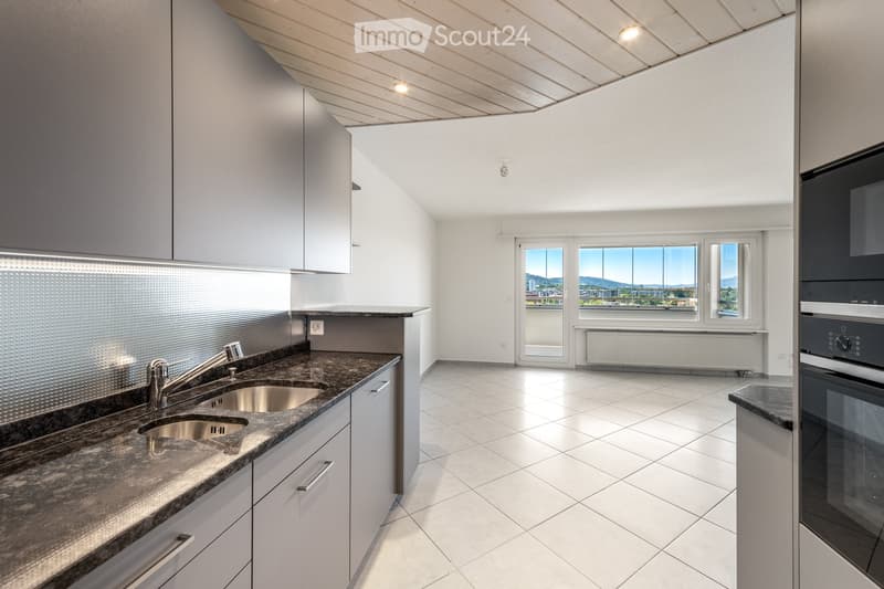 Modern kitchen with white cabinets, granite countertop, stainless steel sink, and built-in oven. Large windows offer a scenic view.