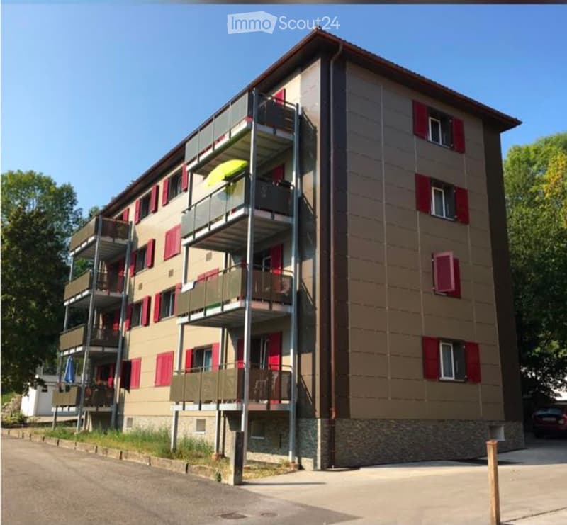 Four-story residential building with multiple balconies, red shutters, and a modern facade.