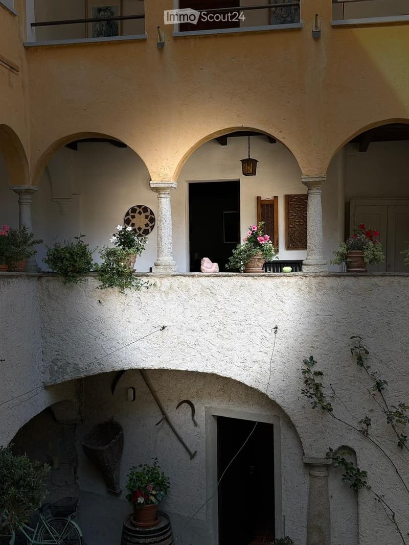 Balcony with arched columns, potted plants, a wicker basket, a bicycle, and a barrel.