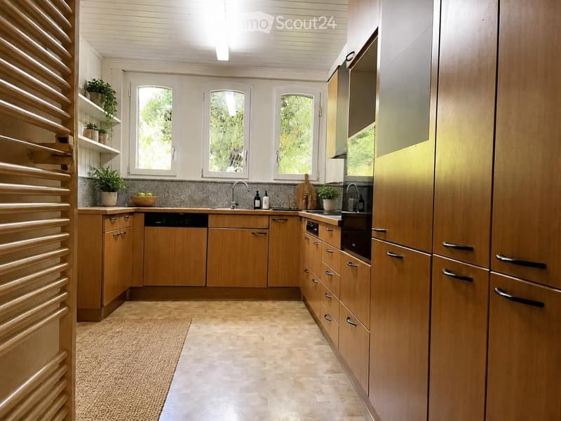 Modern kitchen with wooden cabinets, stainless steel appliances, and a central island. Features a sink, oven, dishwasher, and various kitchen items on the counter.