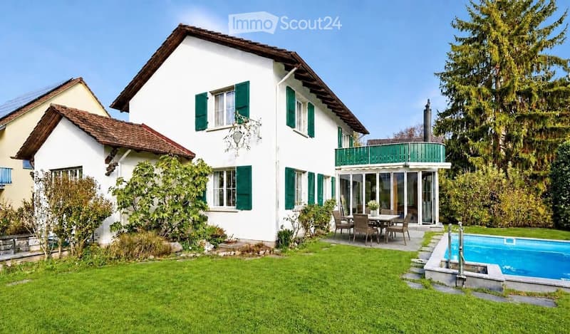 Two-story white house with green shutters, a balcony, a swimming pool, and a well-maintained lawn.