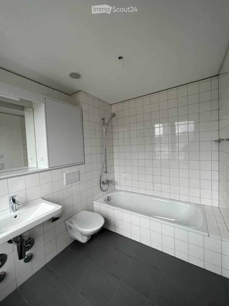 Modern bathroom with white tiled walls and floor, featuring a sink, mirror, cabinet, toilet, bathtub, and showerhead.