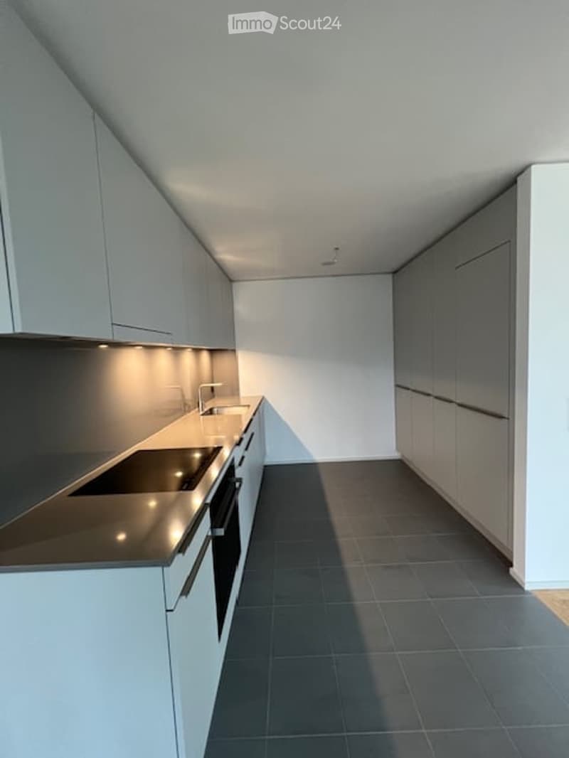 Modern kitchen with white cabinets, black countertops, and a built-in oven. The space features sleek, contemporary design with integrated lighting and a dark tiled floor.